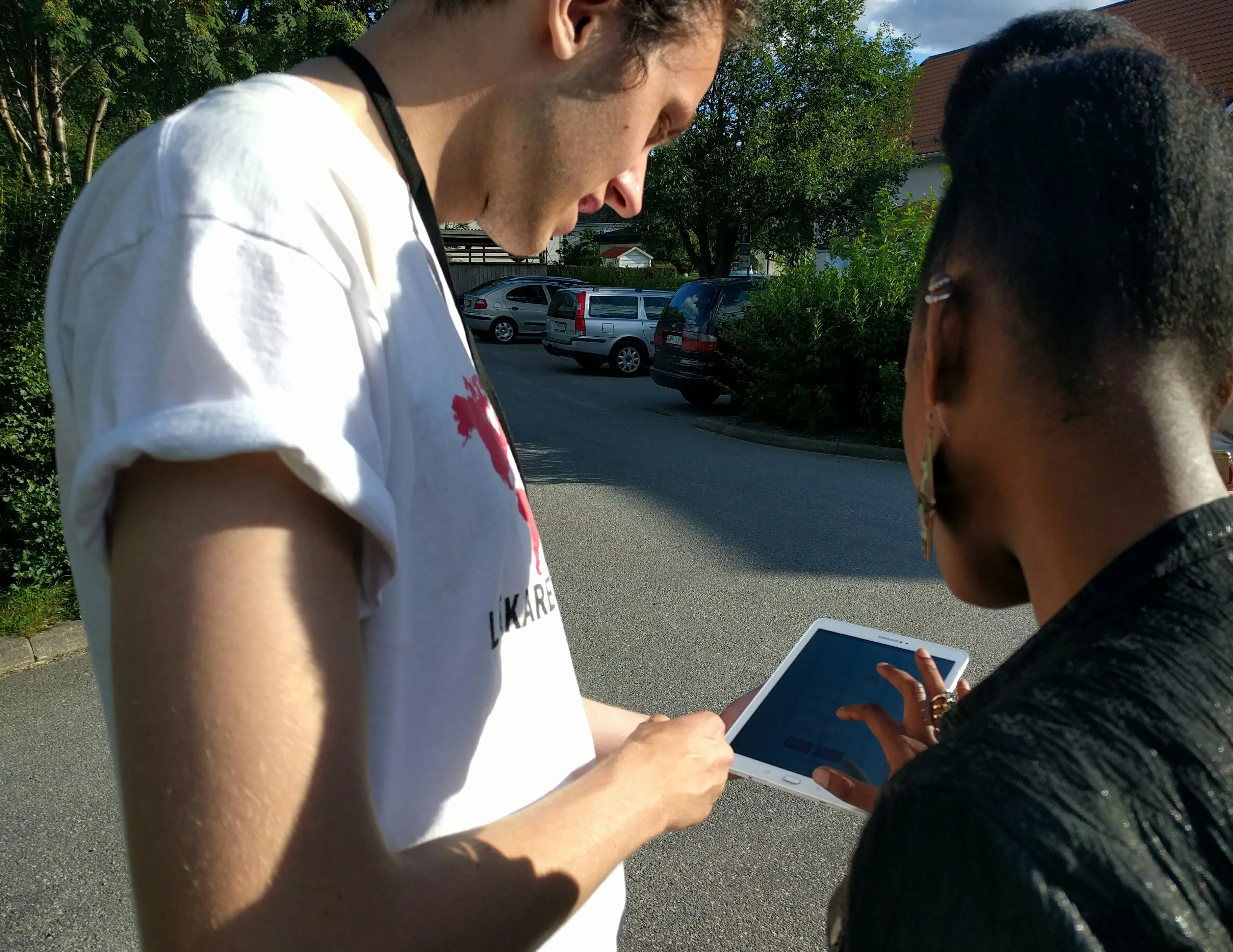 Two field recruiters in Läkare Utan Gränser t-shirts looking at a tablet on a sunny street